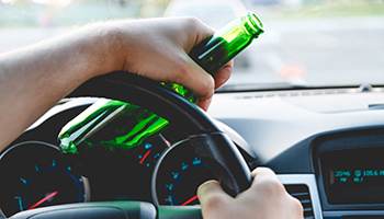 A person gripping a beer bottle while driving a car